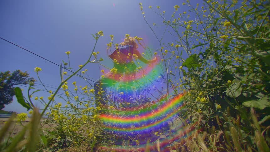 A woman dances on a patch of wildflowers under a clear blue sky on a sunny day with iridescent colorful reflections