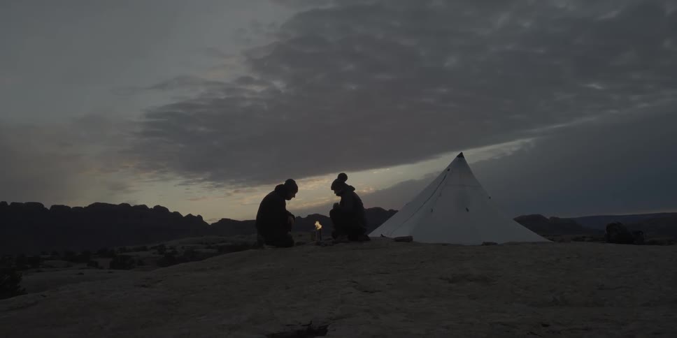 Two people camping and sitting near small fire on windy night,