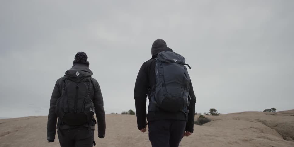 Two people wearing backpacks hike uphill