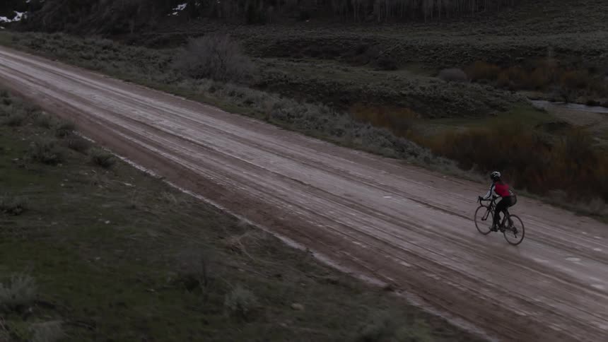 A person rides a bike along a muddy dirt road