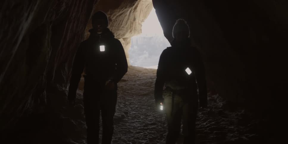 Couple walking into a cave like area with their lights hanging from their chests