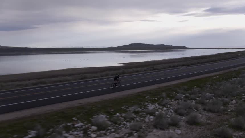 Cyclist riding quickly along a road next to the sea
