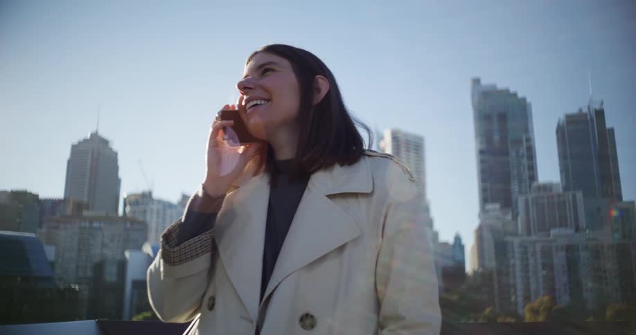 Woman talks on the phone while standing in front of a metropolis under a clear blue sky