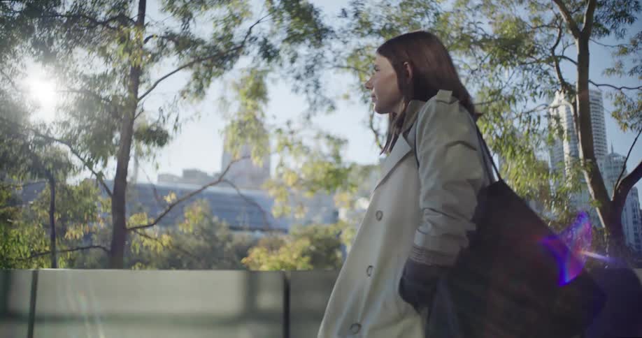 A woman walking in an urban park with skyscrapers in the background