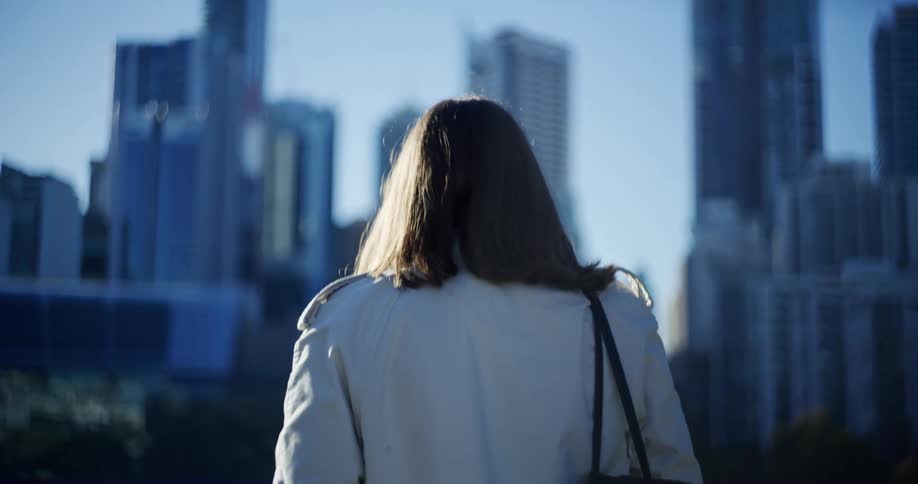 Woman from the back with a white coat and a bag walking in a metropolis