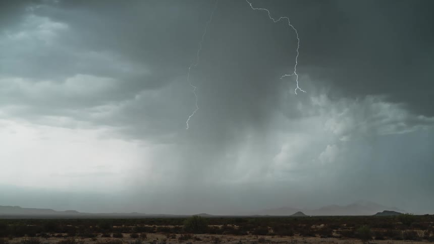 A lightning strike pierces through dark stormy skies illuminating the landscape below