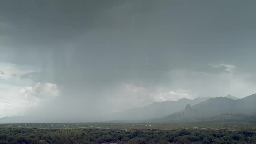 Field with mountains in a cloudy sky with lightning