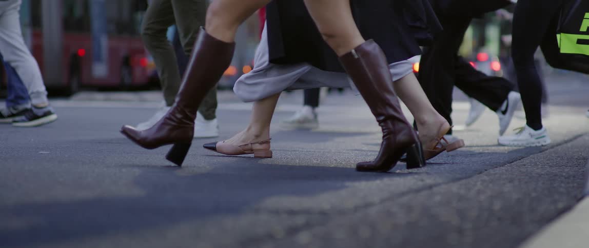 The legs of many people who are crossing an asphalt street