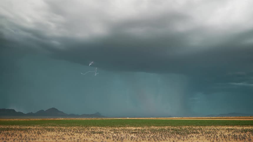 A large storm flashes lightning over mountains and a plain