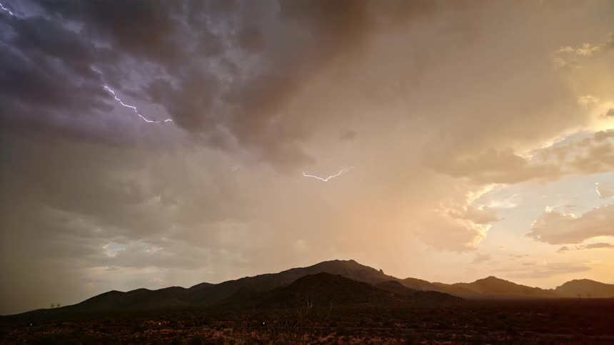 A lightning storm in a mountainous region with a clear orange sky