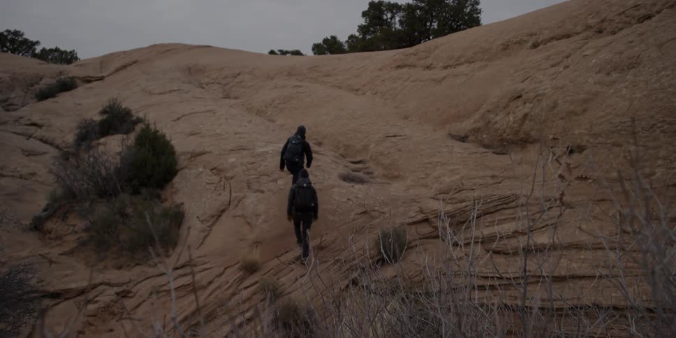 Two people hike up the hillside on a cloudy day
