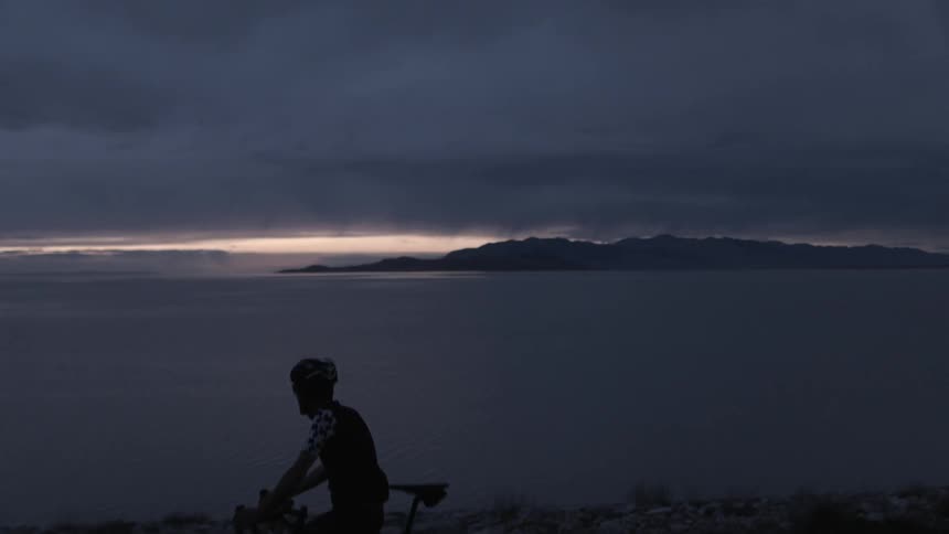 Person sitting waterside on their bicycle looking out at a very cloudy horizon