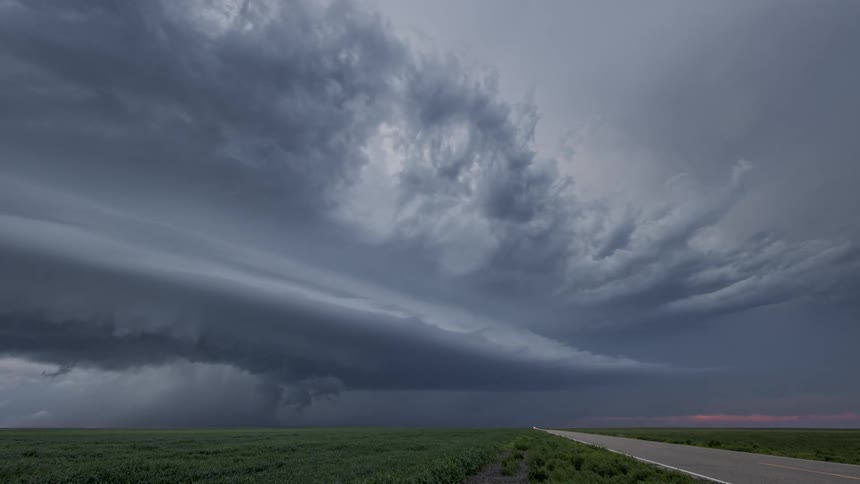 Highway with vehicle traffic on the edge of a greenish field and a sky with a storm of black clouds