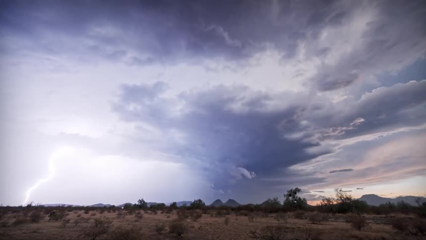 A dramatic desert landscape with storm clouds and several visible lightning strikes in the distance