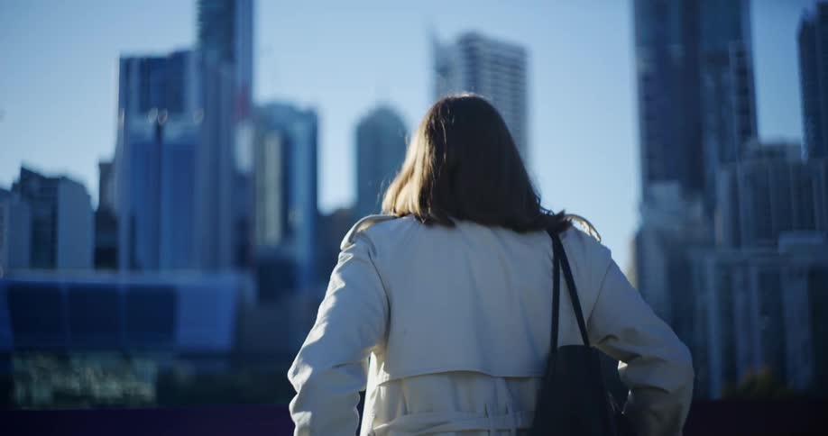 A woman wearing a coat steps outdoors to look at the city skyline