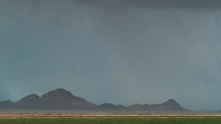 Landscape of a field with the silhouette of mountains in the background in a cloudy sky with lightning