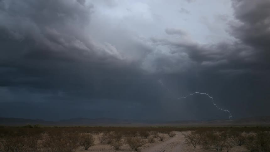 Dark clouds unleash large lightening bursts over mountains and a desert