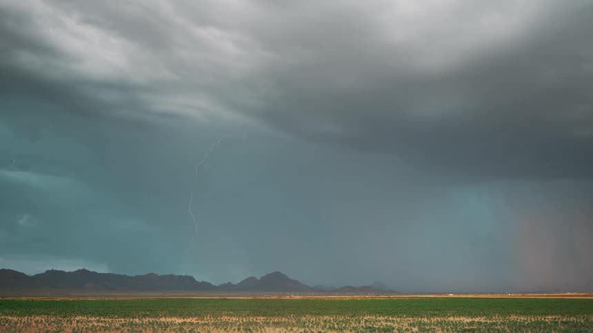 Landscape of a greenish field with silhouette of mountains on the horizon and a day with lightning and rain