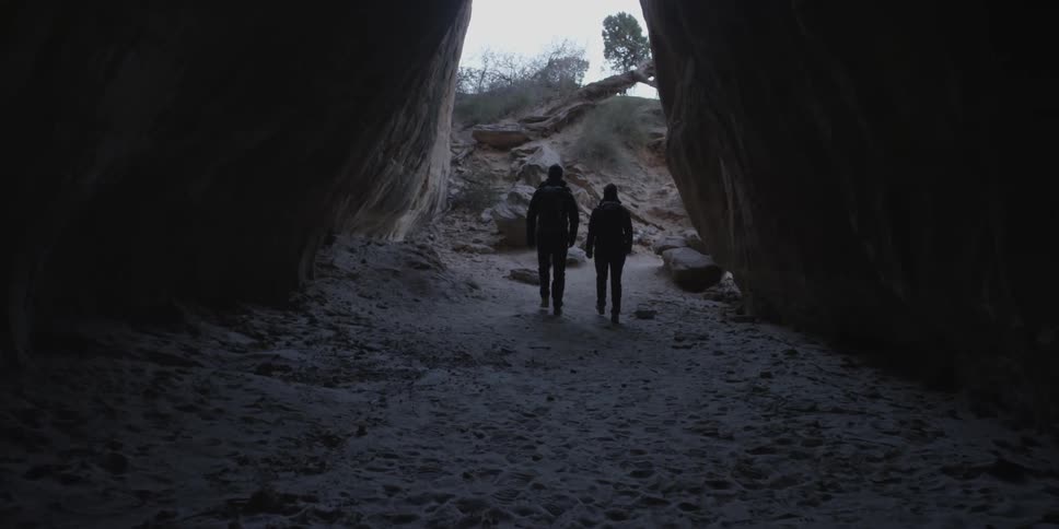 Two people hike out of a dark cave