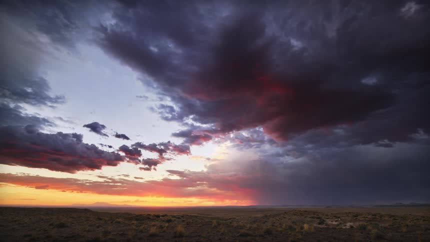Dark clouds move over a vast grassy plain at dusk