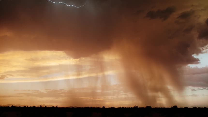 Multiple lightning bolts illuminate red tinted storm clouds moving across the silhouetted landscape