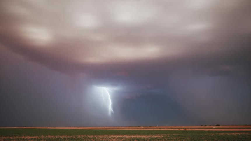 A lightning storm spans a field under a large gray cloud with glowing white spots