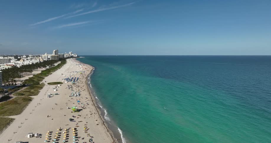 A beach with clear turquoise waters and a shoreline dotted with colorful beach umbrellas and sun loungers
