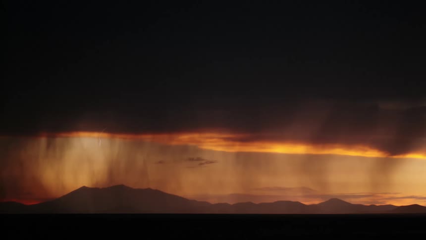 Lighting and rain over the silhouette of mountains at dusk