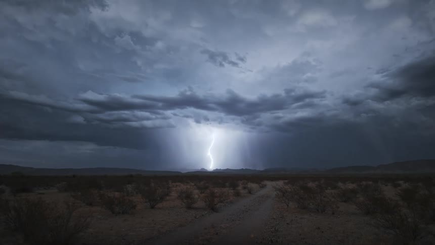 A lightning strike pierces through dark stormy skies illuminating the landscape below