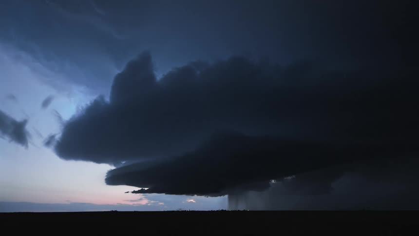 A large storm cloud emits a lightning strike that flashes in the dark sky