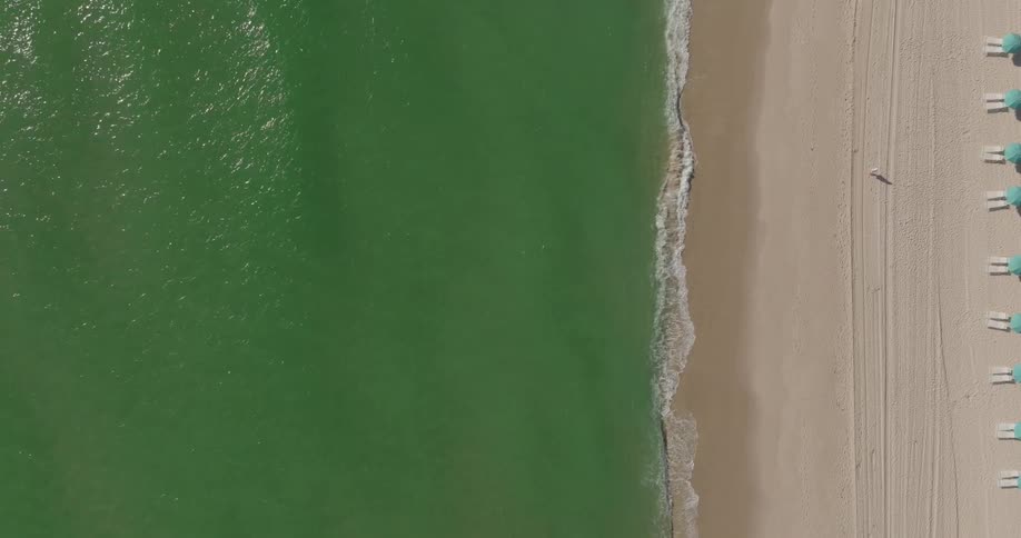 Several beach chairs are lined up on a beach as ocean waves wash ashore