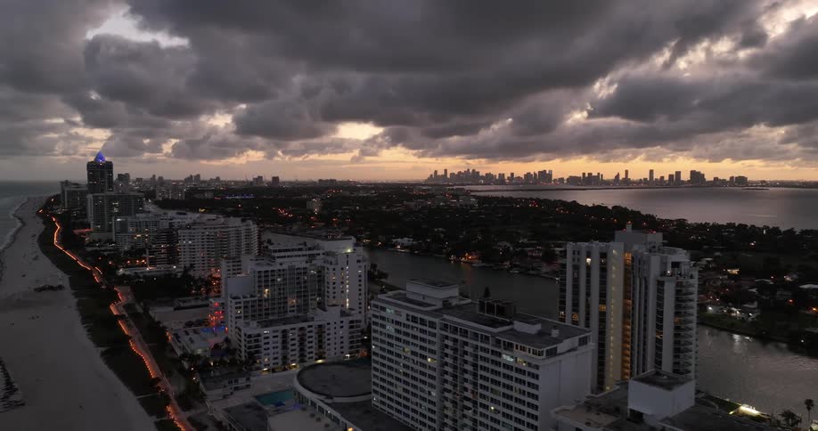 Water separates midrise buildings from forested neighborhoods on a peninsula with city skyline silhouetted against a red tinted sky in the background