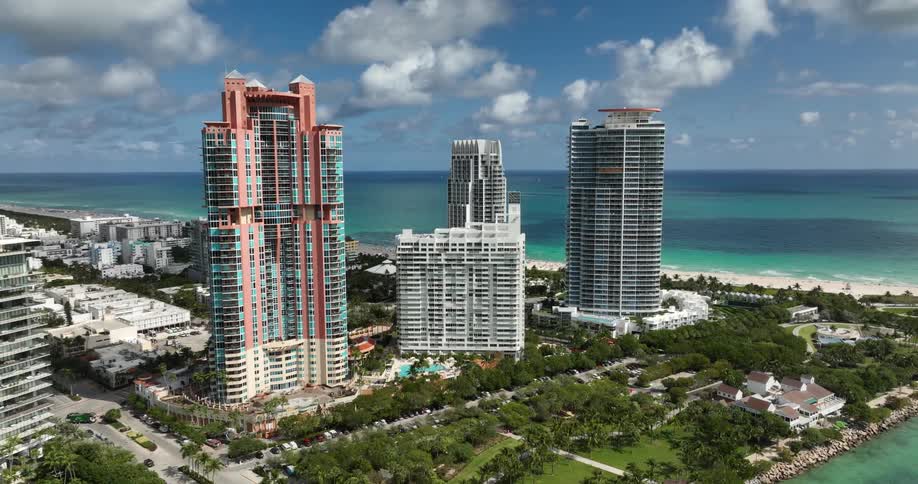 A highangle view of a coastal cityscape with three prominent skyscrapers near a turquoise sea