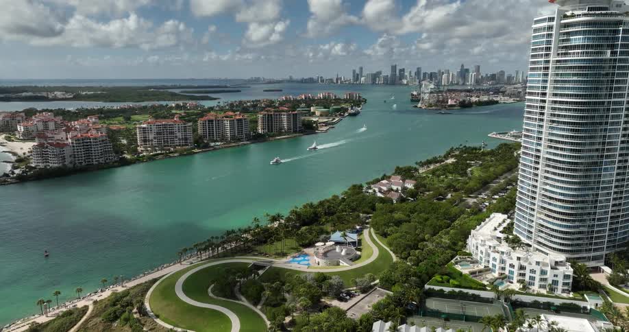 Multiple boats move through the water between coasts lined with housing a distance from the city skyline on the horizon