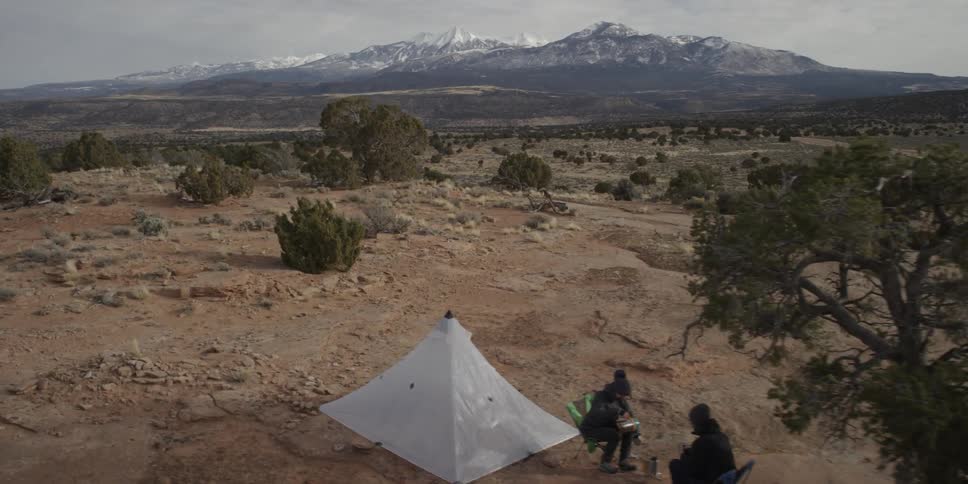Two people are sitting outside a tent in a scenic landscape