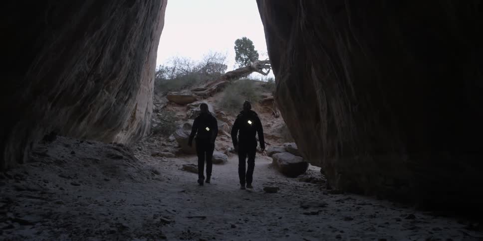 Couple walking into a cave like area with their lights hanging from their chests