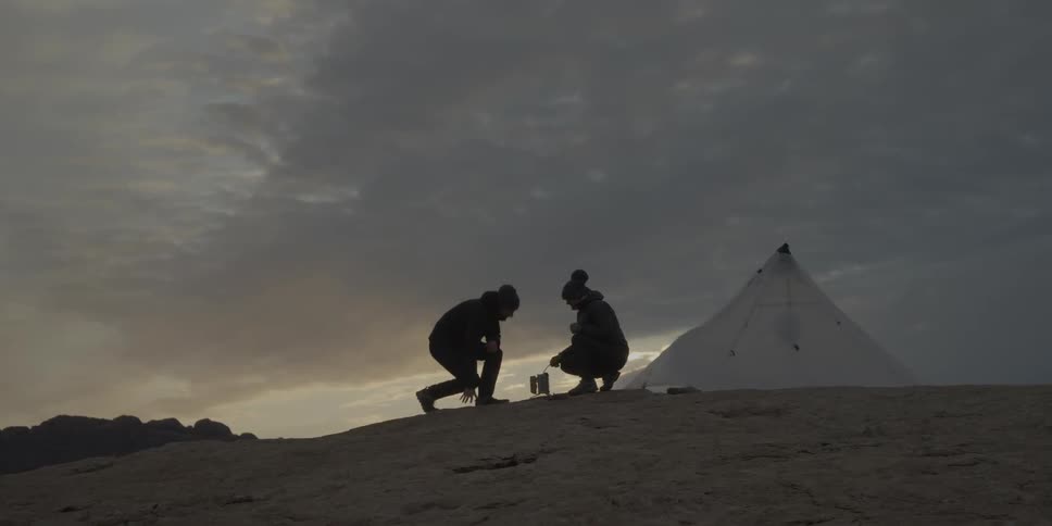 People starting a fire outside their tent on a windy  and cloudy  day at sunset
