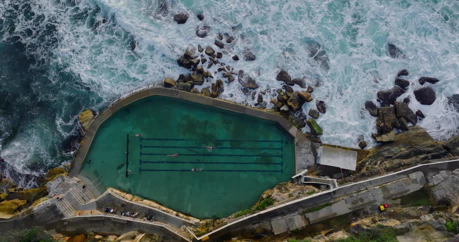 Swimmers in a lap pool bordering the ocean and spectators off to the side