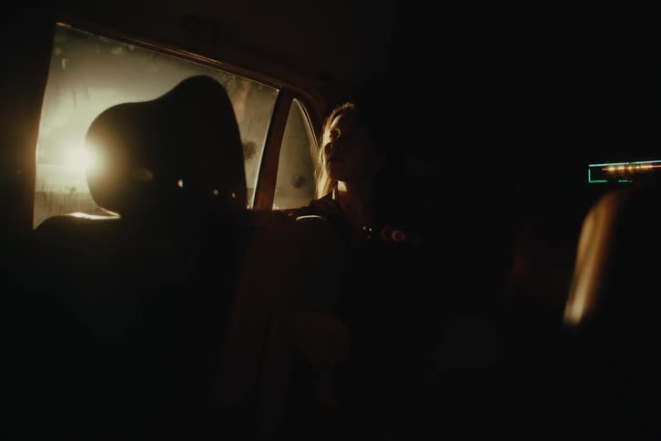 A woman sits in the backseat of a car as the sun shines through the window
