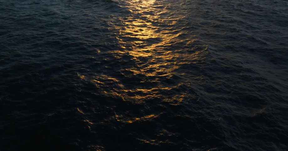 Waves move across an ocean surface while reflecting the sun