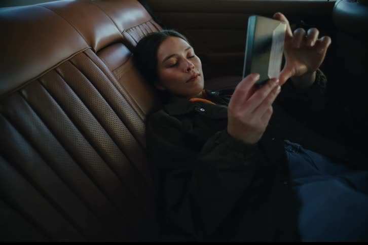 Young woman lying on a leather seat in the car watching and holding a floppy disk