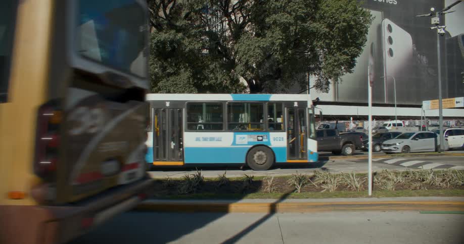 A blue bus and a yellow bus passing through a street full of cars