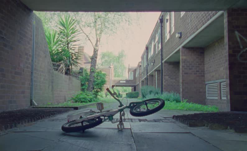 A bicycle with a spinning wheel sits on pavement outside of an apartment building