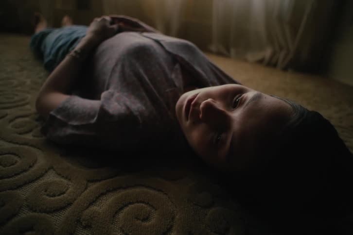 A woman is lying on a carpet on the floor and looking to her left side