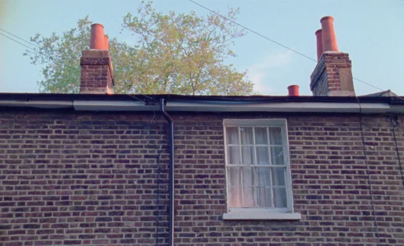 Light shines through a curtained window in the brick wall of a house on a cloudy day