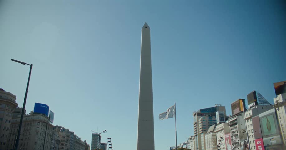 Flag and a white obelisk stand between apartment buildings near downtown on a windy day