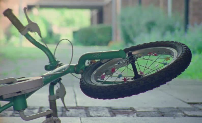 A green children bicycle lies on its side the front wheel spinning