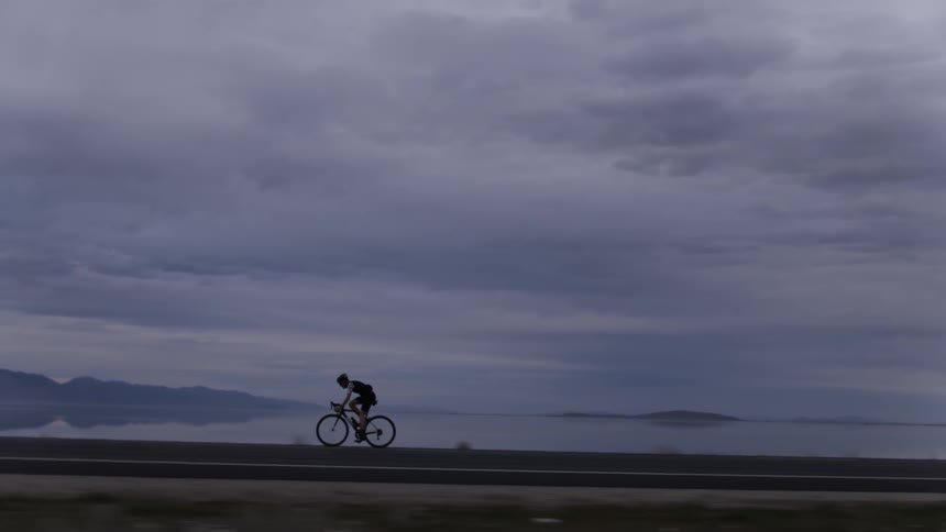 Person riding a bicycle on a highway near a lake