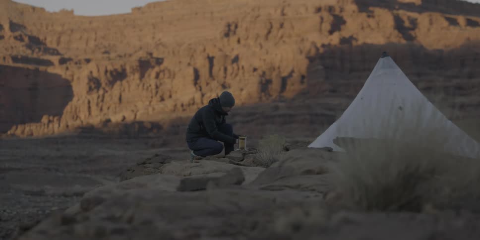 Man starting a fire next to his  tent in the wilderness