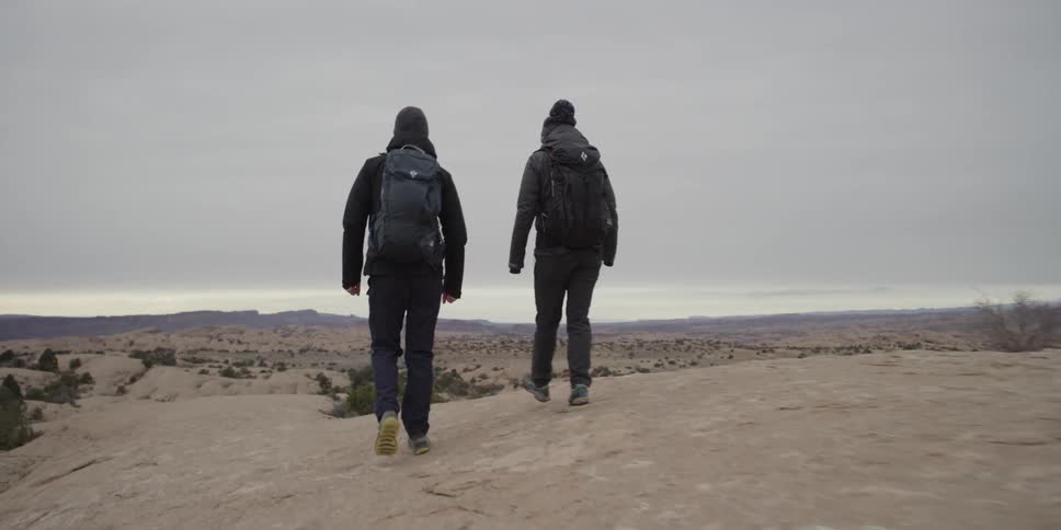 Two people wearing backpacks hike a hill top